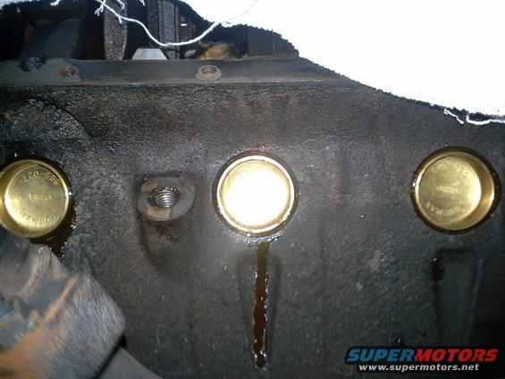 Close-up of an engine block showing three brass freeze plugs, one with visible part number 170-595