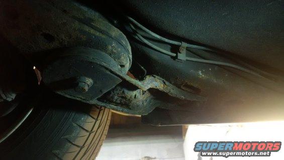 Undercarriage of a vehicle showing extensive rust on the frame and suspension components, with a tire visible