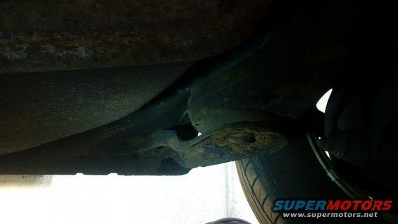 Undercarriage view of rusted metal and suspension components, with a tire visible