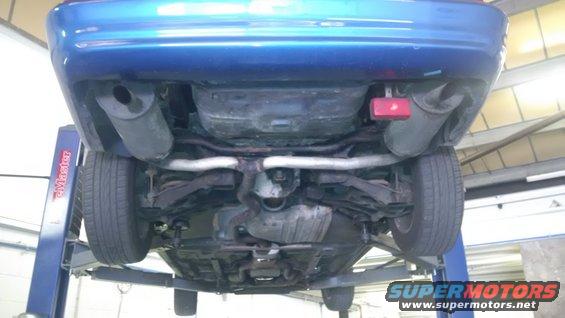 Underside of a blue car on a lift, showing the exhaust system and suspension components
