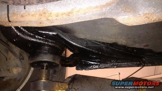 Undercarriage of a vehicle with black undercoating applied to the frame and suspension components. A jack is visible supporting the frame