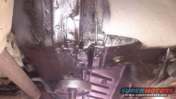 Vehicle underbody with black undercoating, showing a rusty exhaust pipe and part of the frame