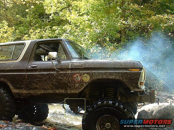 Muddy 1978 Ford Bronco driving through water with smoke coming from engine