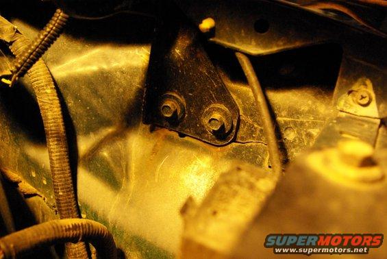 Close-up of a metal bracket with two bolts, next to a ribbed wiring harness in an engine bay