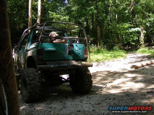 Green off-road vehicle with a roll cage, driving on a dirt path in the woods