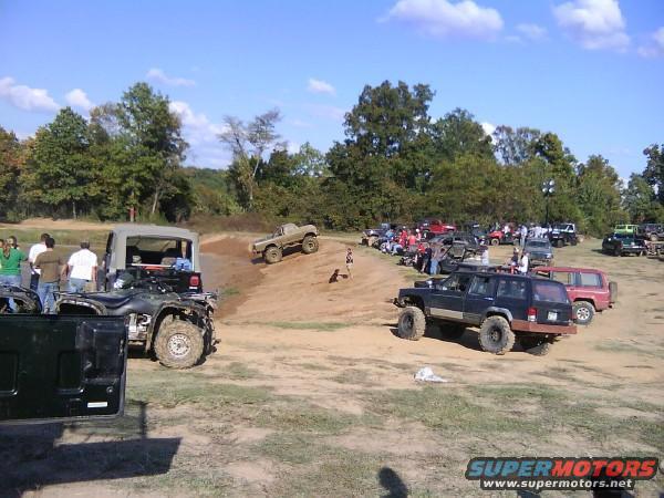 Off-road vehicles gathered on a dirt lot with trees in the background