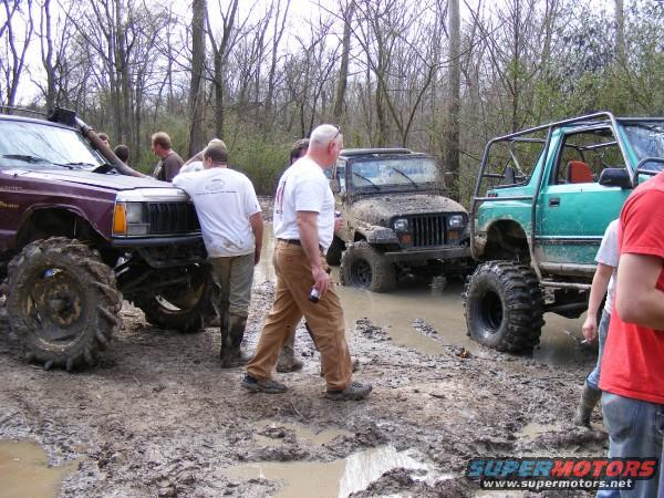 Several modified off-road vehicles stuck in thick mud with people around them