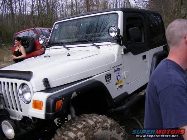 White Jeep Wrangler with black soft top, mud on tires. Red Jeep visible behind it