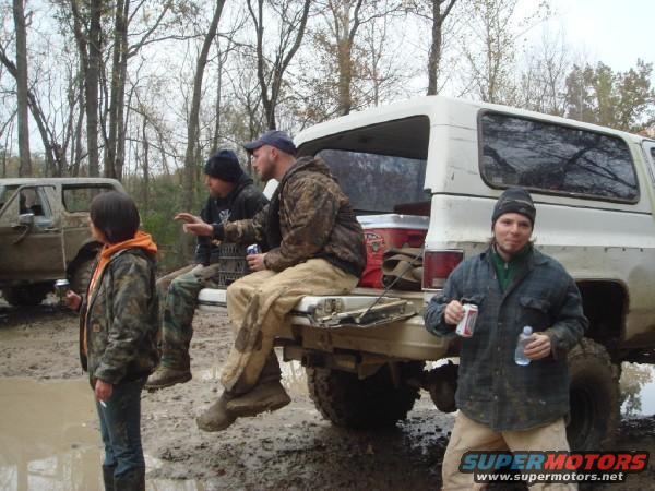 White SUV rear view with people in the bed, muddy terrain