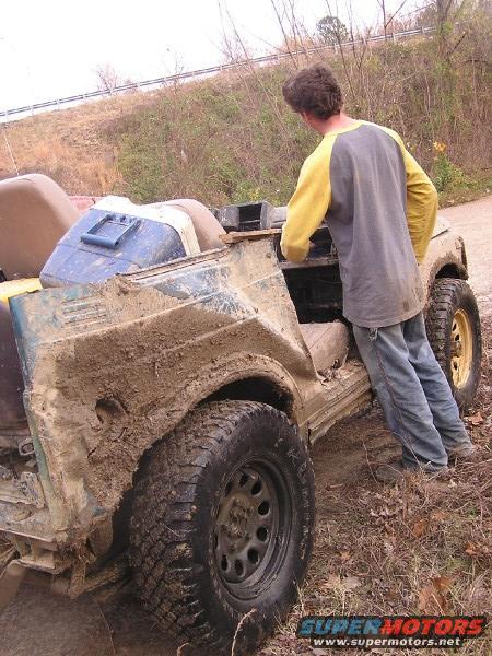 Muddy off-road vehicle with a person standing next to it, looking into the open top