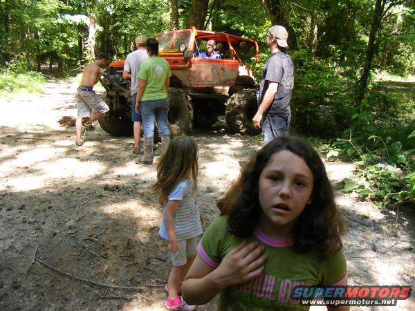 Orange off-road buggy with people gathered around in a wooded area