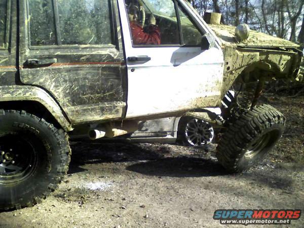 Muddy Jeep Cherokee XJ with large tires, driver visible inside