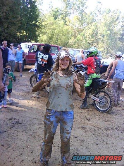 Mud-covered woman with hands up, dirt bikes and people in background