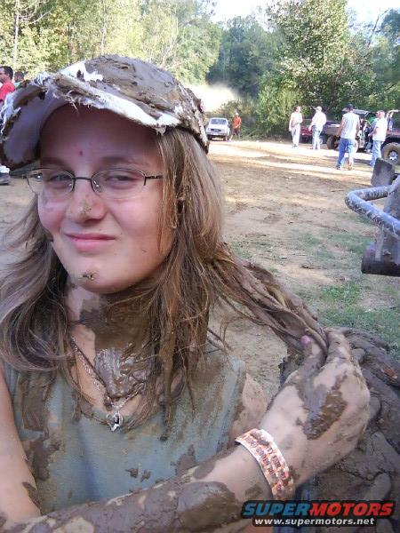 muddy person in foreground, several vehicles in background at an outdoor event