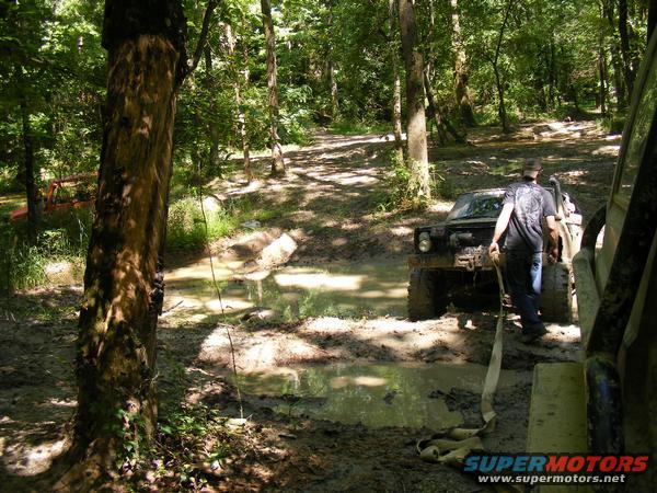 Off-road vehicles stuck in mud on a forest trail, one vehicle being pulled by a strap