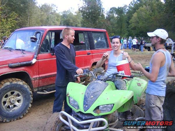 Red SUV with snorkel, green ATV, and three people in muddy outdoor setting