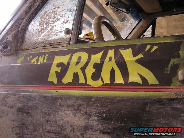 Side view of a dirty off-road vehicle with "THE FREAK" painted in yellow on the door