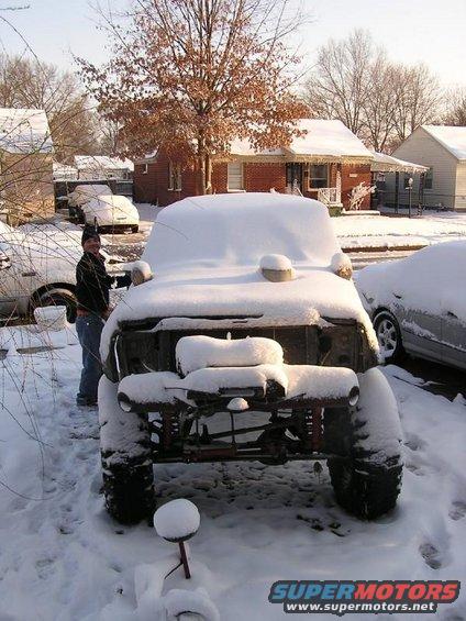 Person standing next to a heavily snow-covered off-road vehicle with large tires