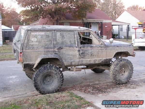 Mud-covered Jeep Cherokee XJ with oversized tires parked on a residential street