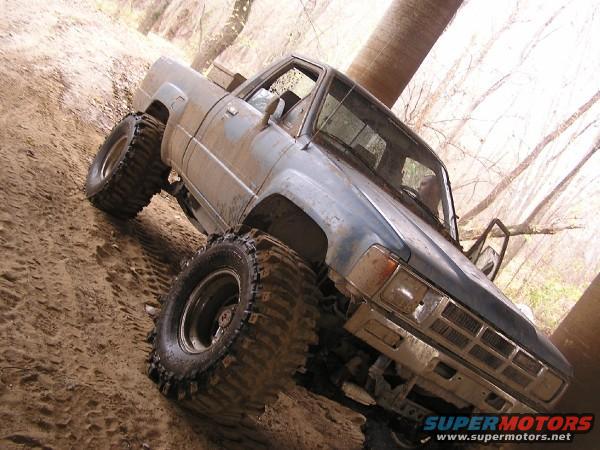 Muddy blue pickup truck with oversized tires on a dirt trail