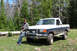 1989 Ford Bronco - A man leans against a white and dark blue Ford F-Series truck in a wooded area.
