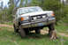 1989 Ford Bronco - Ford Bronco navigates an obstacle on a dirt road, with one front wheel elevated on a tree stump.