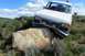 1989 Ford Bronco - A white Ford truck is stuck on a large rock with a person visible in the cab.