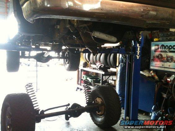 Truck chassis on a blue lift, showing suspension and undercarriage. The front axle is removed