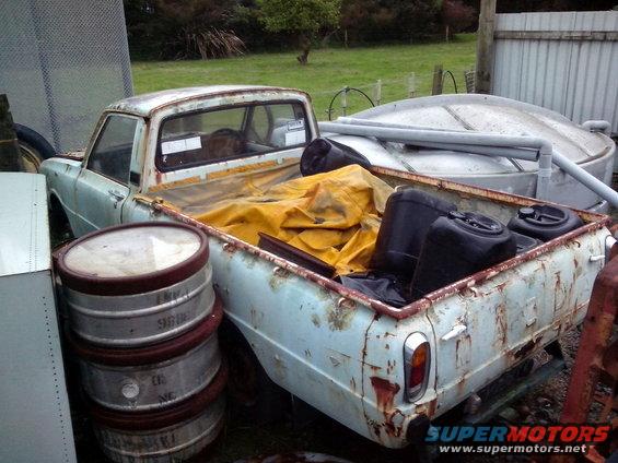 Rear view of a light blue pickup truck loaded with barrels and containers