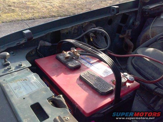 Engine bay with red car battery and visible Supermotors.net watermark