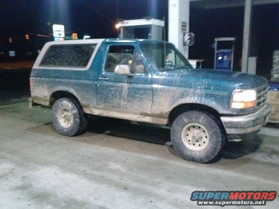 Mud-splattered teal 1992 Ford Bronco with a white top, seen at a gas station