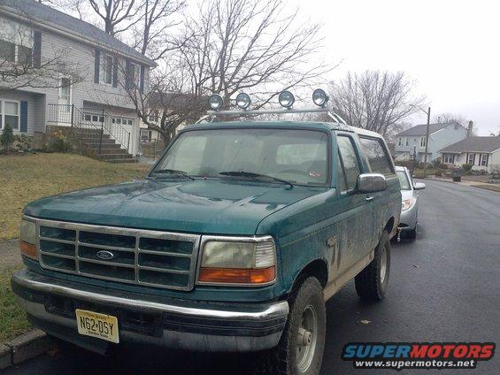 Green 1996 Ford Bronco parked on a residential street, equipped with a roof-mounted light bar