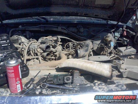 Engine bay with tools and a removed air filter. A can of cleaner is on the left