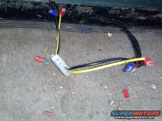 Vehicle wiring harness with yellow and black wires, connectors, and a gray junction block on carpeted floor