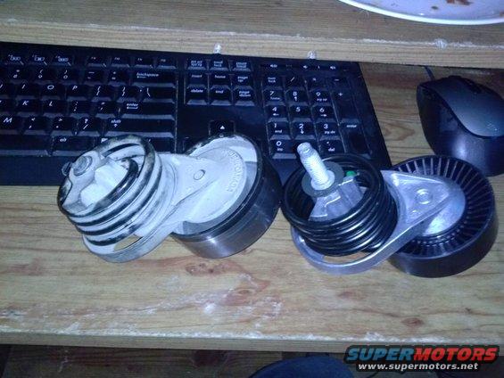 Two belt tensioner pulleys on a wooden surface with a keyboard and mouse