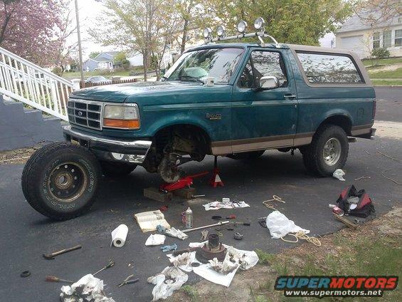 Green 1996 Ford Bronco with front wheel off, undergoing maintenance