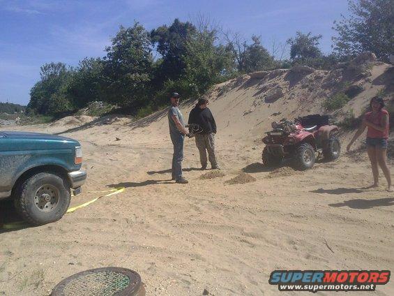 Green pickup truck front view, red ATV in sandy area with people