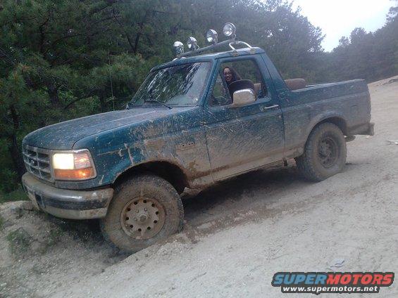 Muddy teal 1996 Ford Bronco with roof lights driving off-road