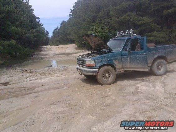 Green pickup truck with hood open on a muddy road