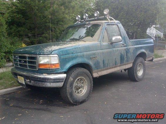 Teal Ford Bronco with roof-mounted lights and aftermarket wheels, covered in dirt