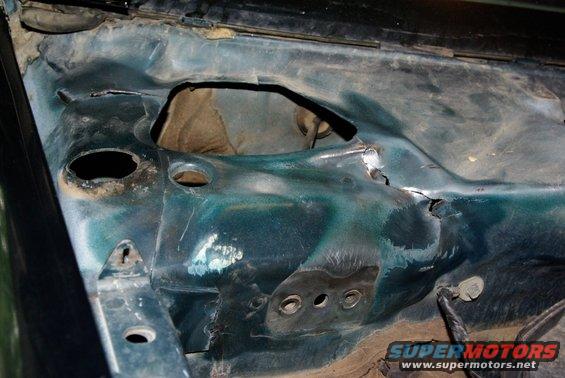 Close-up of a vehicle's firewall with holes and some rust