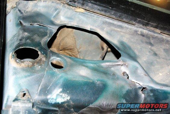 Damaged green car hood interior with rust and large holes