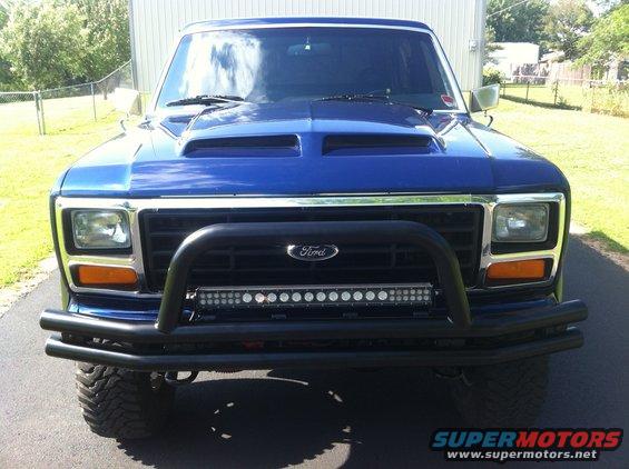 Front view of a blue Ford Bronco with a custom hood scoop, bull bar, and LED light bar