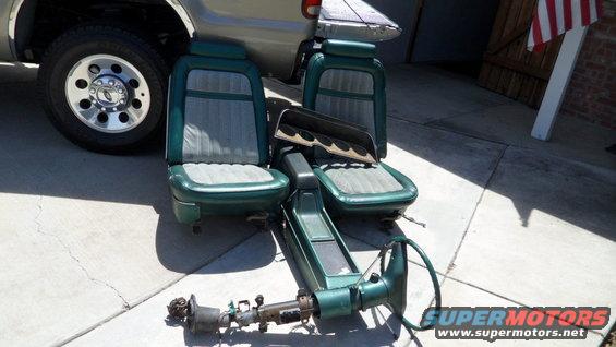 Green car seats and a steering column assembly on a concrete surface next to a truck tire