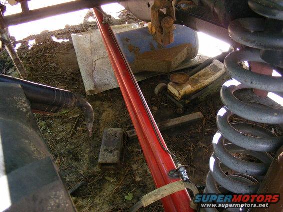 Close-up of a red suspension component, large coil spring, and various debris under a vehicle