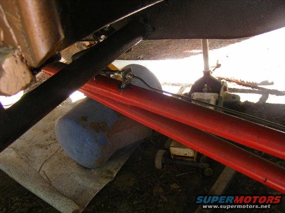 Undercarriage of a vehicle with bright red suspension arms and black frame components, supported by a jack