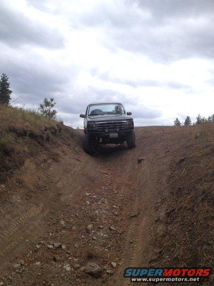Black off-road vehicle driving up a steep dirt incline under a cloudy sky