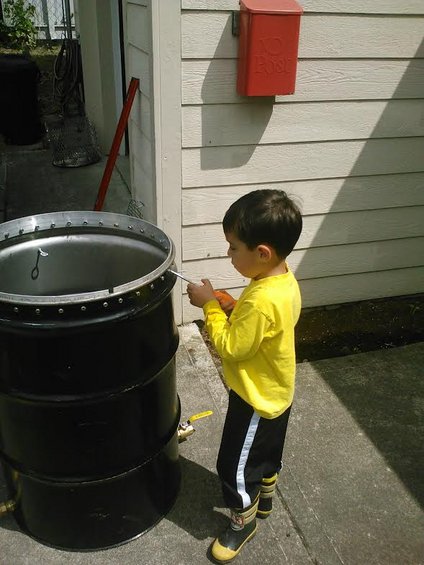 Kid in yellow shirt and boots next to a big black barrel