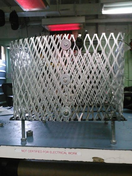 Metal cage with diamond pattern, mounted on legs, with red heat lamps overhead