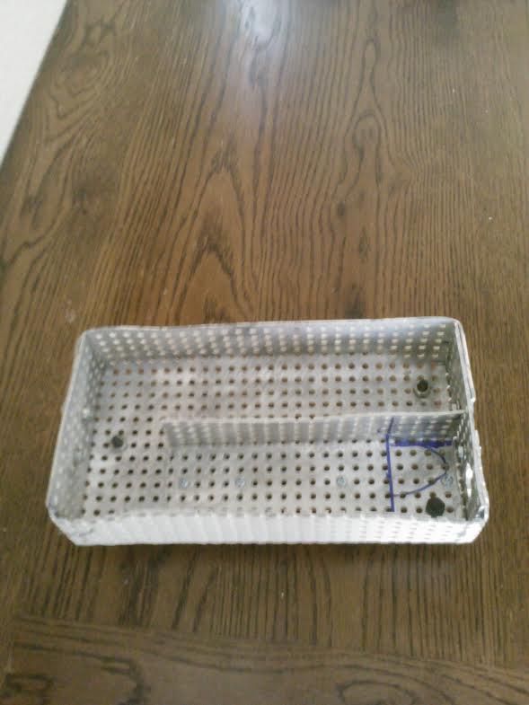 Perforated metal tray with a divider and blue markings on a wooden table